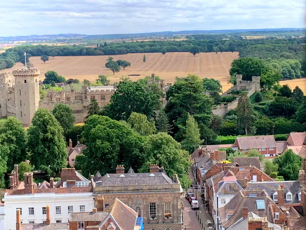 Warwick Castle seen from St Mary's church tower, above the treetops with farmland behind